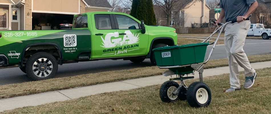 Green Again professional applying granular fertilizer from spreader to lawn in Castleton, IN.